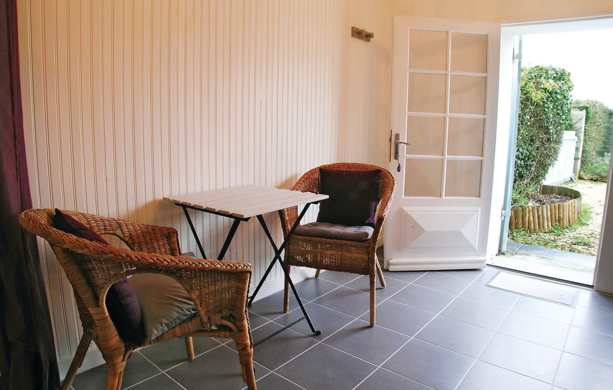 Um quarto pequeno com uma cadeira de vime, uma mesa e uma porta de vidro deslizante que dá para um jardim.