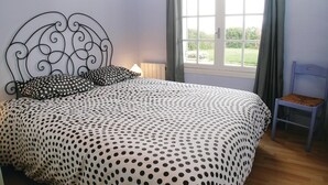 Un dormitorio con cama, una silla, una ventana con cortinas y vistas a la vegetación.