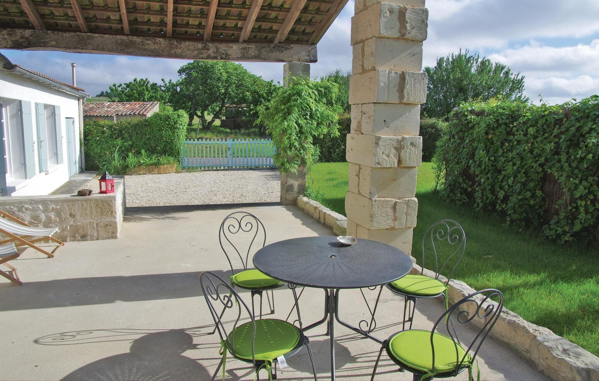 An outdoor patio with a round table and four chairs, a stone pillar, and a view of a house and garden.