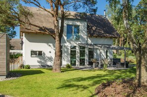 A modern two-story house with a large patio area, a covered outdoor seating space, and a well-maintained lawn.