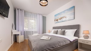 Ein modernes Schlafzimmer mit einem großen Bett, einem Nachttisch mit Lampe, einem kleinen Schreibtisch und einem Gemälde eines Leuchtturms an der Wand.