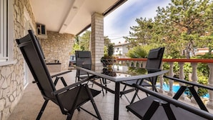 Eine Terrasse im Freien mit Tisch und Stühlen, Steinmauern und Blick auf ein Schwimmbad und Bäume.