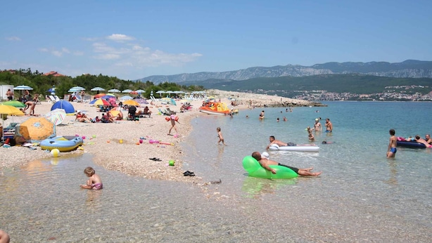 Ein Strand mit badenden und entspannenden Menschen, Sonnenschirmen und Liegestühlen.