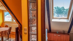 Une pièce avec un plafond en pente, un coin repas avec une nappe à carreaux et une vue par la fenêtre.