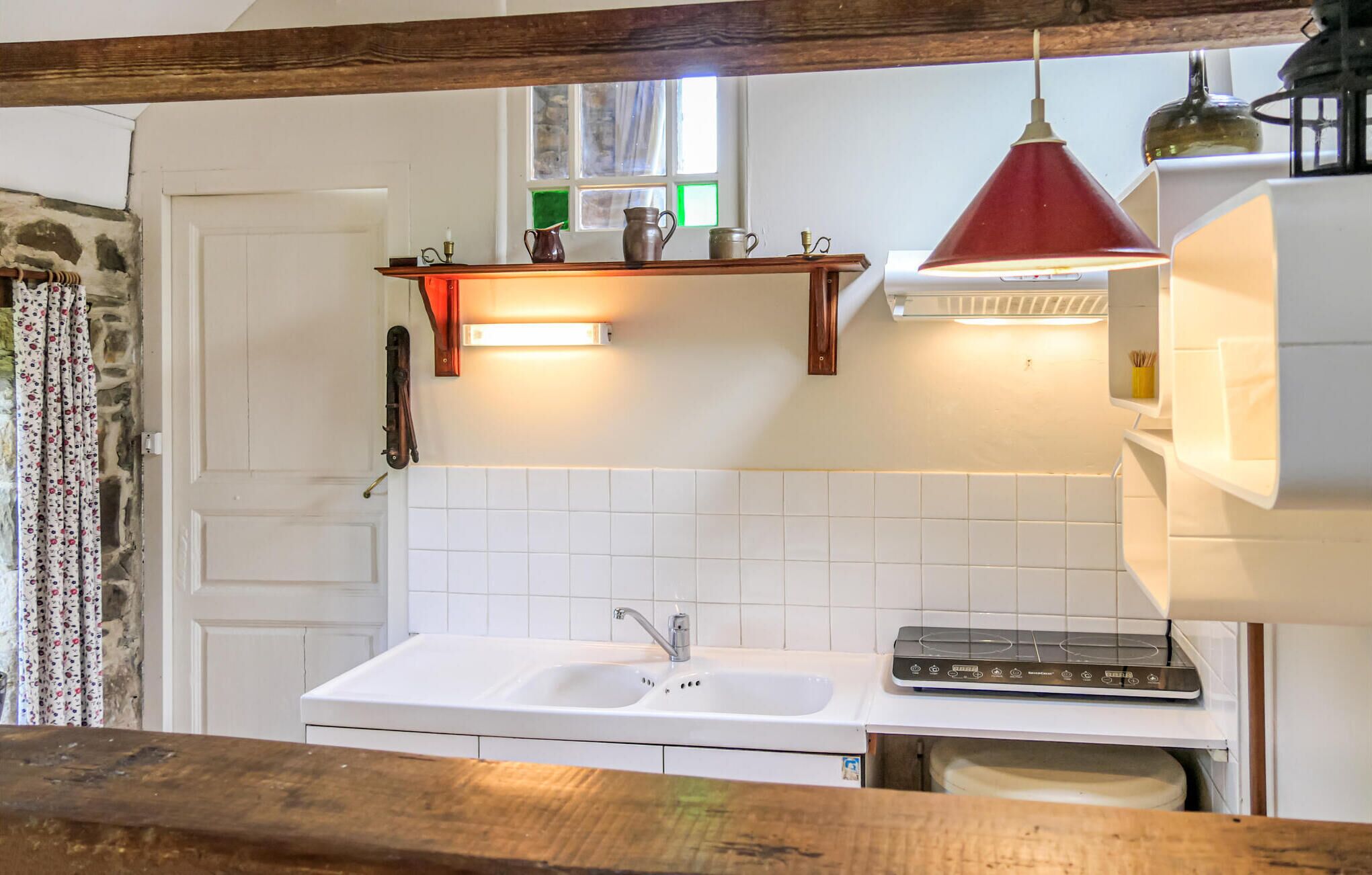 A kitchen with a white sink, a stove, and a hanging red pendant light.