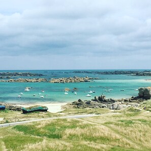 A coastal landscape with rocky outcrops, a sandy beach, and boats in the water.