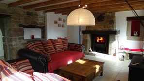 Un salon chaleureux avec une cheminée en pierre, un plafond en bois et un canapé rouge agrémenté de coussins à rayures.