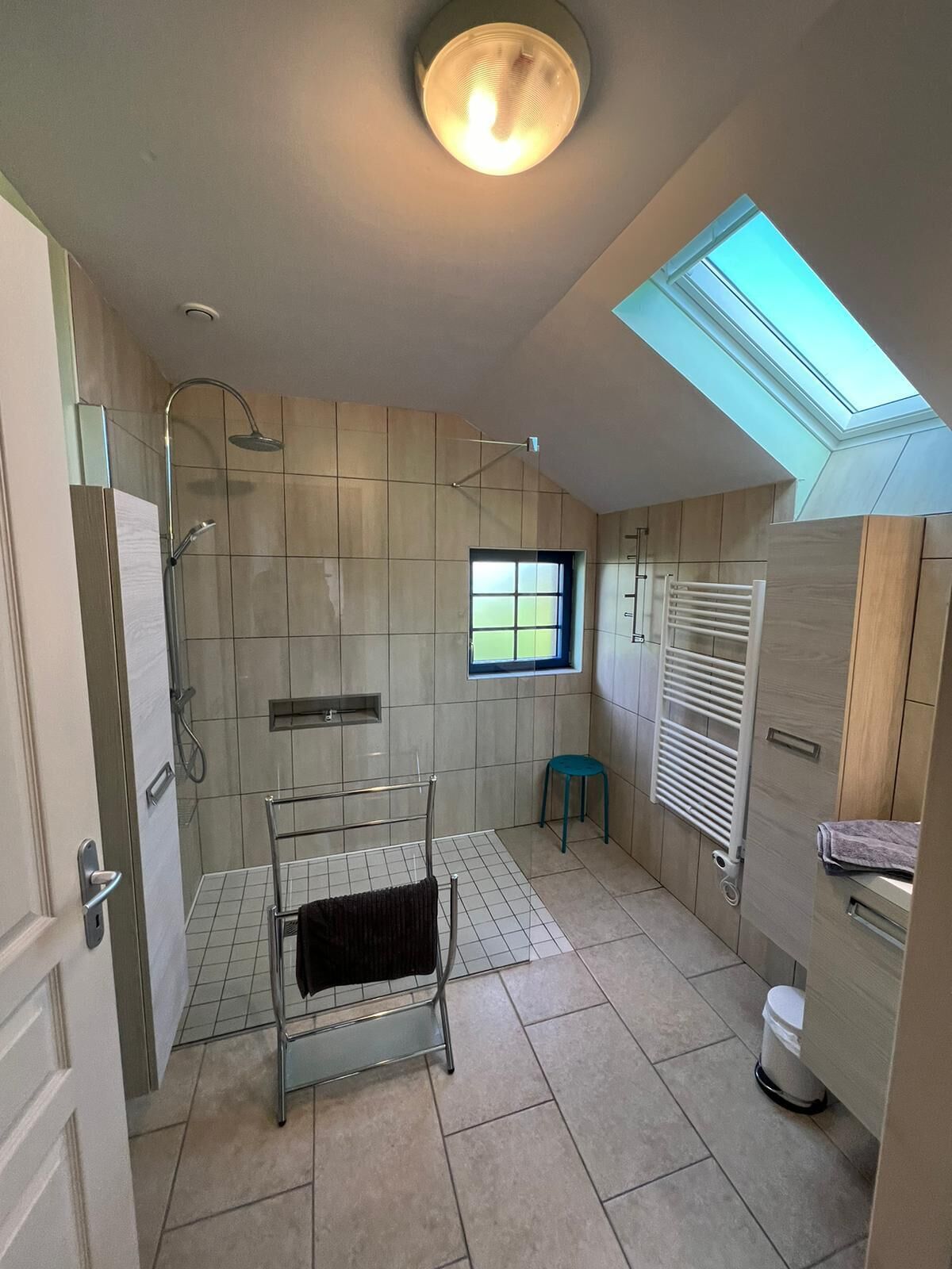 A modern bathroom with a skylight, a shower, a towel rack, and a window.