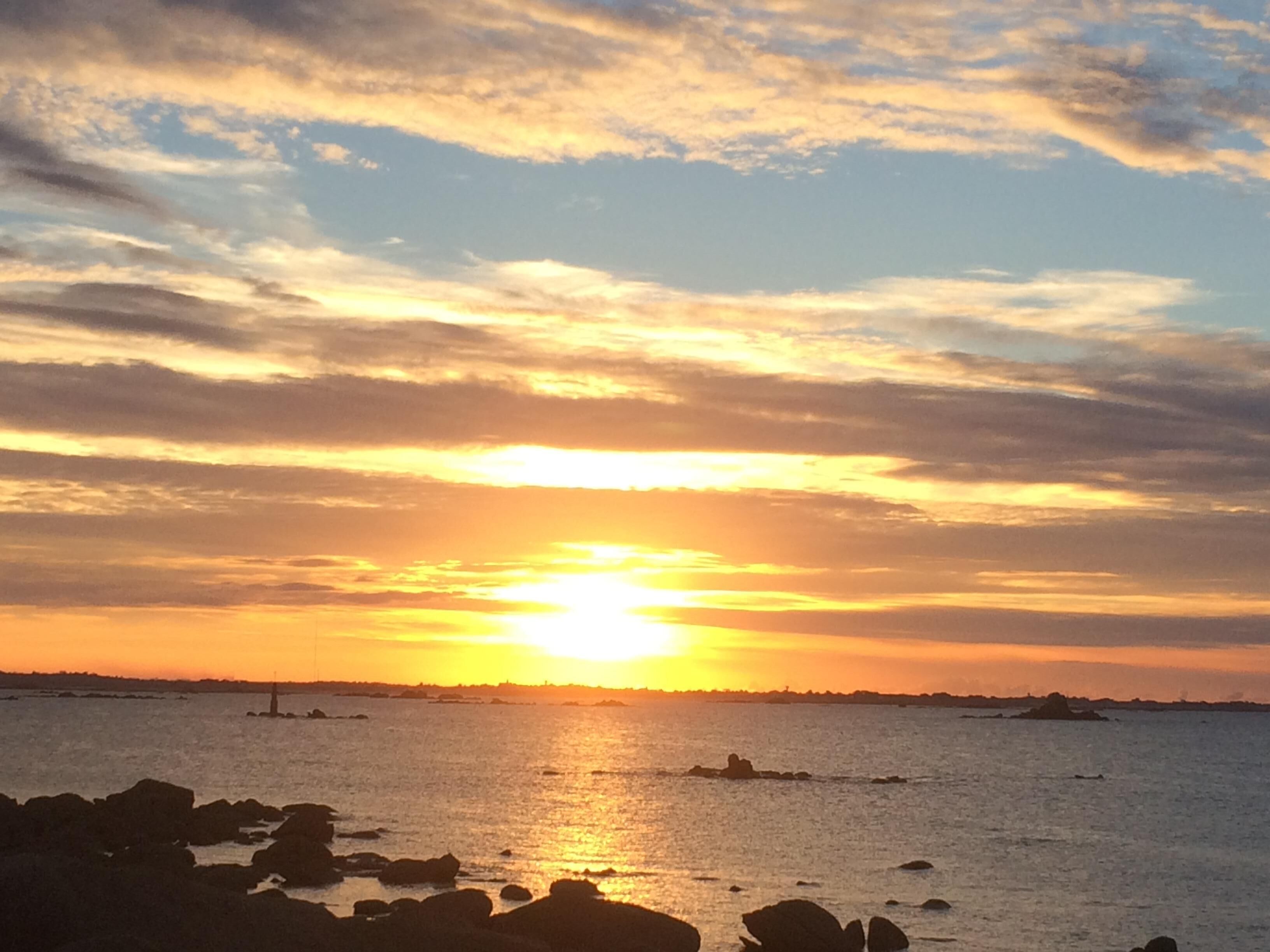 A sunset over a body of water with rocky formations in the foreground.