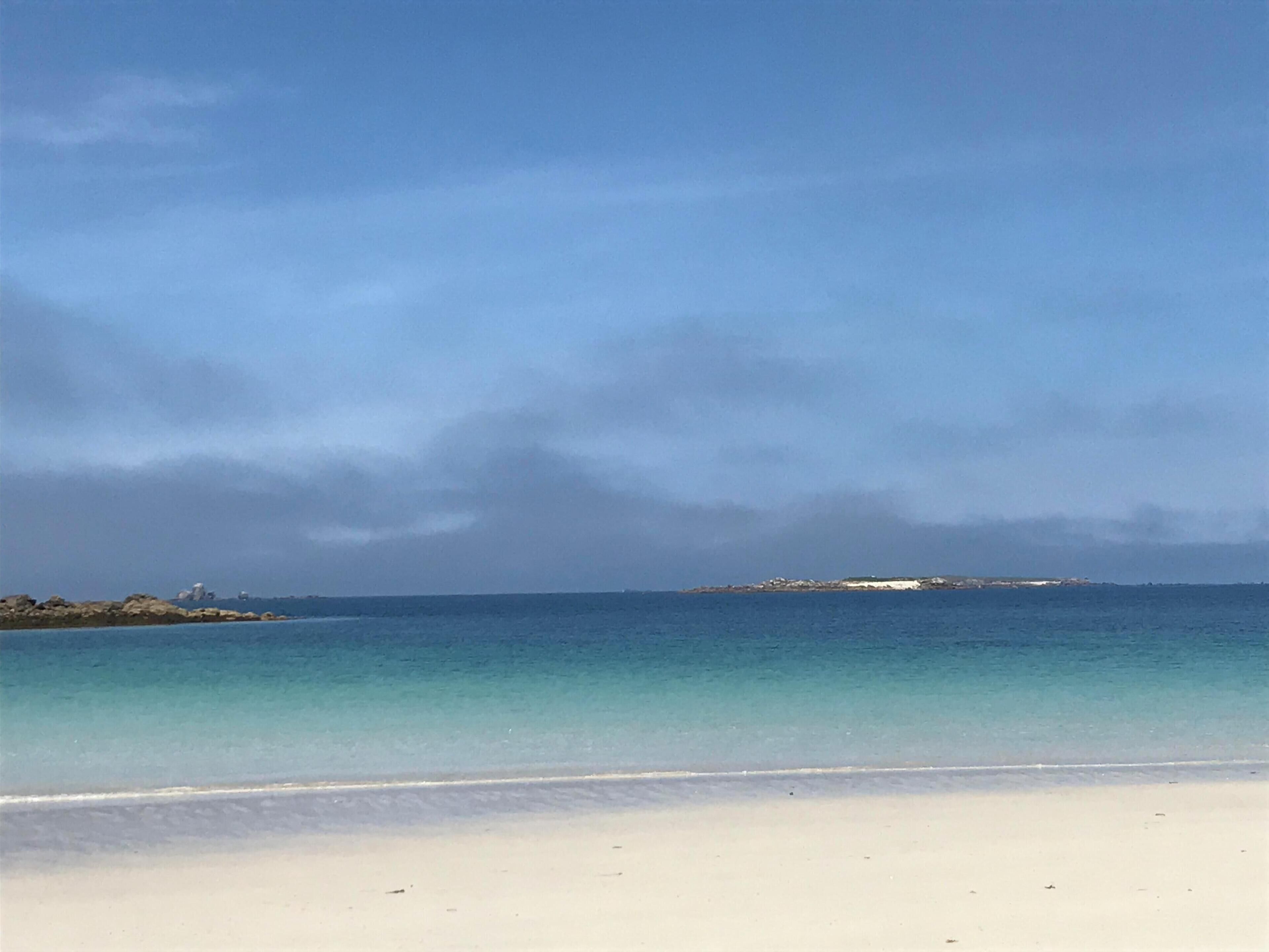 A beach with clear water, a sandy shore, and a distant island.