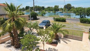 A residential area with a parked car, palm trees, and a view of a lake with boats. - Nice home in Le Grau d'Agde (Le Grau d'Agde)
