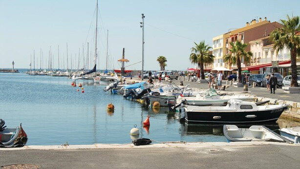 A marina with boats docked along the waterfront, a pedestrian walkway, and buildings with balconies. - Nice home in Le Grau d'Agde (Le Grau d'Agde)