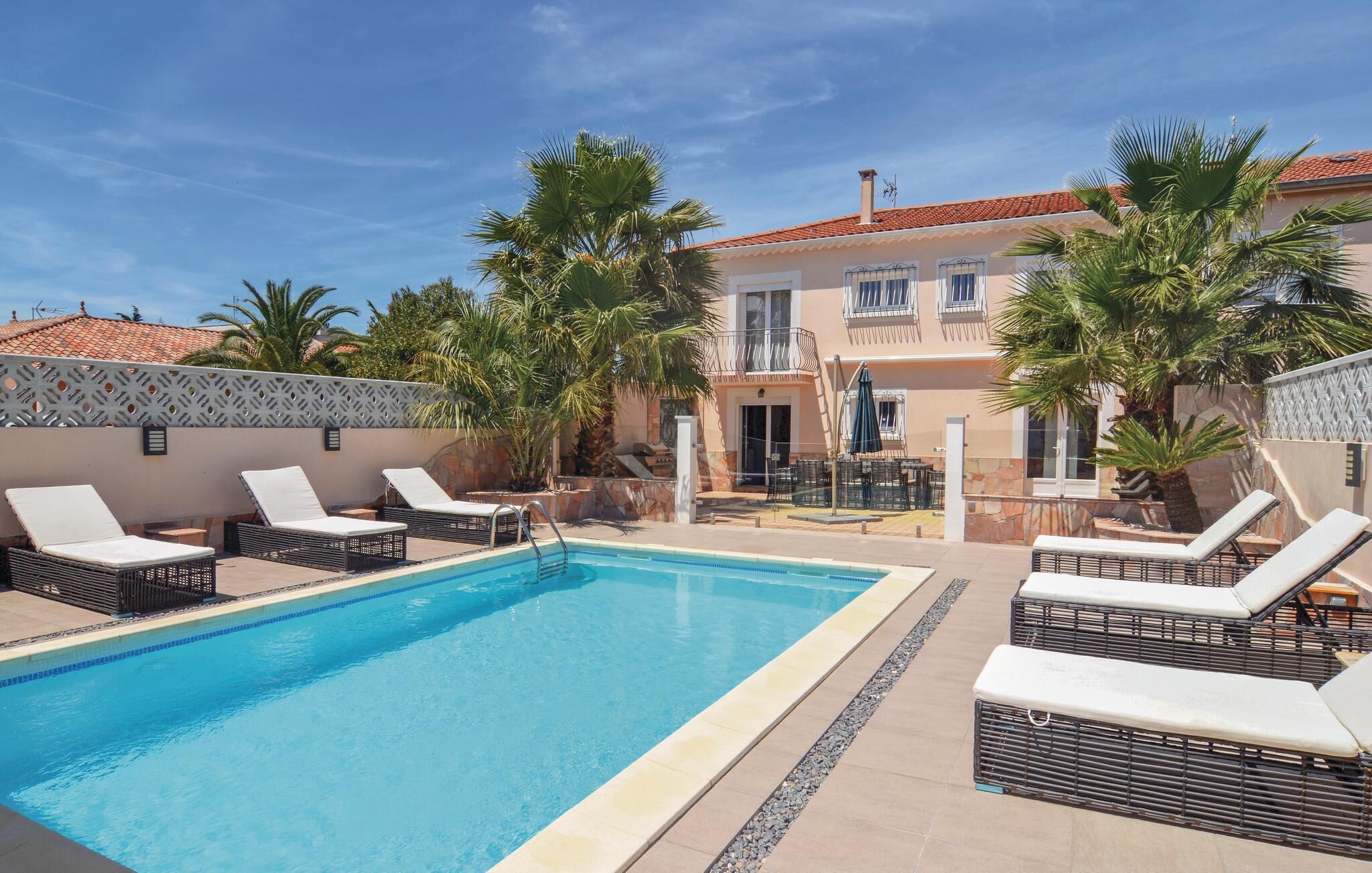 A pool area with lounge chairs, a pool, and a building with a tiled roof.
