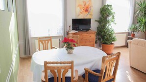 Un coin repas avec une table ronde, des chaises en bois, un téléviseur posé sur un meuble et des plantes en pot.