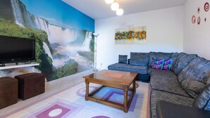 A living room with a large waterfall mural, a flat-screen TV, a sofa with colorful cushions, and a coffee table. - Amazing apartment in Kleke with WiFi (Kleke)
