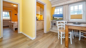 A bright yellow room with wooden flooring, a dining table with chairs, and a view of the beach through a window. - App.9 - Priel Hüs, Germany (List)