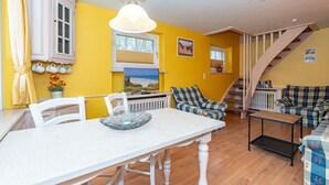 A bright yellow room with a dining table, chairs, a sofa, and a staircase. - App.9 - Priel Hüs, Germany (List)