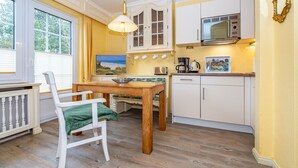 A kitchen with a wooden table and chairs, a microwave, and a window with blinds. - App.9 - Priel Hüs, Germany (List)