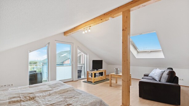 A spacious attic bedroom with a large bed, a wooden TV stand, a sofa, and a skylight. - Beach front home in Süssau/Ostsee (Süssau/Ostsee)
