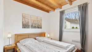 A bedroom with two beds, wooden headboard, a window with curtains, and artwork on the wall. - Beach front home in Süssau/Ostsee (Süssau/Ostsee)