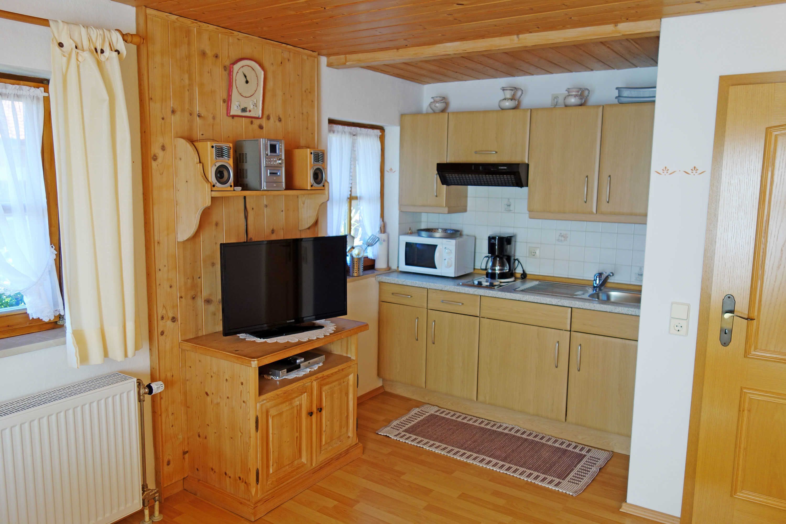 A compact kitchen with wooden cabinets, a microwave, a coffee maker, and a television on a wooden stand.