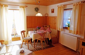 Une pièce chaleureuse aux murs en bois, avec une table à manger et des chaises, un banc et une fenêtre agrémentée de rideaux.