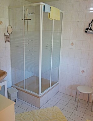 Un baño con ducha de vidrio, lavamanos, inodoro y un pequeño taburete.