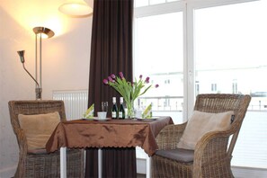 Ein Zimmer mit Korbstühlen, einem Tisch mit brauner Tischdecke, einer Vase mit lila Blumen und einer Lampe.