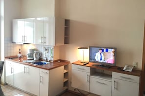 Una cucina con mobili bianchi, una macchina per il caffè, un lavandino e un televisore che mostra una scena.