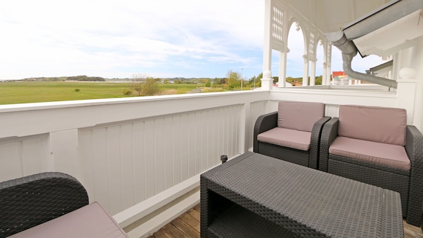 A covered outdoor seating area with wicker furniture and a view of a green field. - F: SEEMANN Apartment Whg. C14 with balcony - SEEMANN Apartment Whg. C14 with balcony - SEEMANN Apartment Whg. (Thiessow)