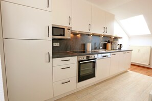Moderni keittiö, jossa on valkoiset kaapit, sisäänrakennettu uuni, mikroaaltouuni ja suuri kattovalokuvio.