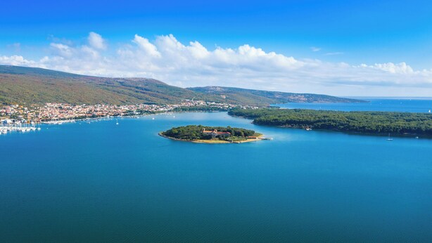Vista aérea de un pueblo costero con una pequeña isla que presenta un edificio destacado.