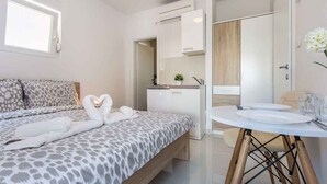 Un dormitorio moderno con cama, mesita de noche, kitchenette pequeña y baño.