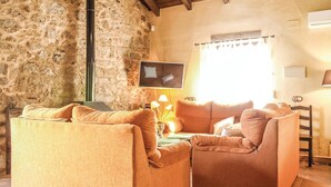 A cozy living room with a stone wall, a flat-screen TV, and a wooden dining table. - Stunning home in Villanueva del Duque (Villanueva del Duque)