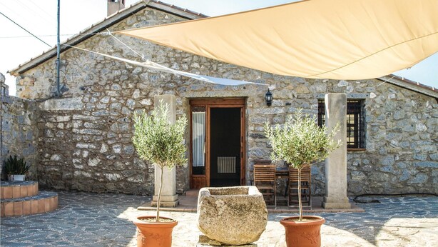 A stone building with a wooden door, two potted olive trees, and a large beige canopy. - Stunning home in Villanueva del Duque (Villanueva del Duque)