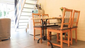 Ein Essbereich mit Holztisch und Stühlen, eine Treppe im Hintergrund und ein Küchenbereich mit einem Mixer auf der Arbeitsfläche.
