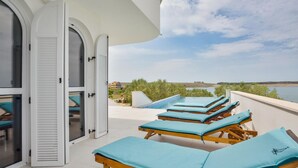 A balcony with sun loungers and a pool, overlooking a body of water and distant buildings.