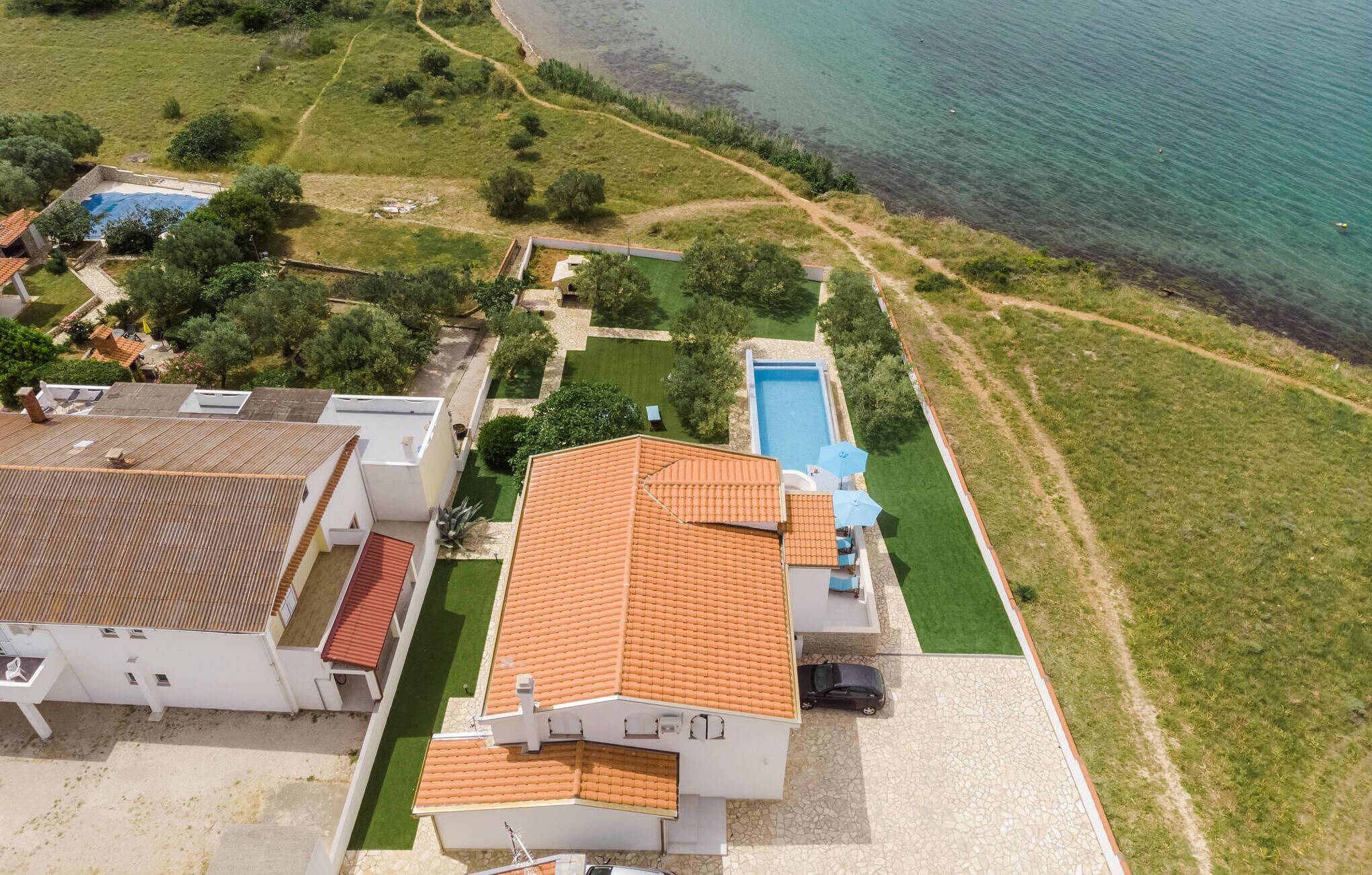 Vue aérienne d’une propriété située sur la côte, avec une piscine, de vastes pelouses verdoyantes et une vue dégagée sur la mer.