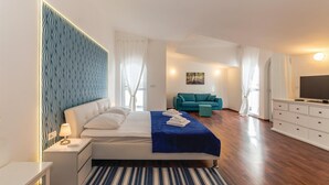 A modern hotel room with a bed, a blue sofa, a TV, and a painting on the wall.