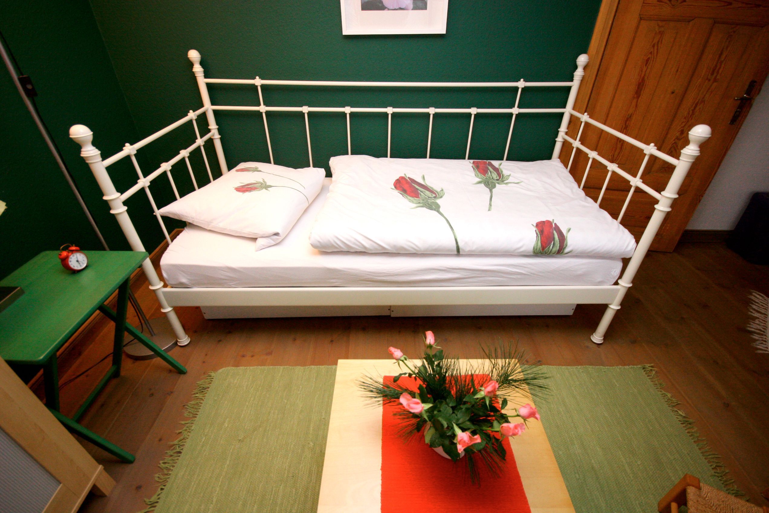 A bed with white bedding and rose patterns, a green wall, and a wooden floor.