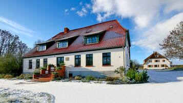 Ein zweistöckiges Haus mit rotem Ziegeldach, zahlreichen Fenstern und einer Ziegelveranda.