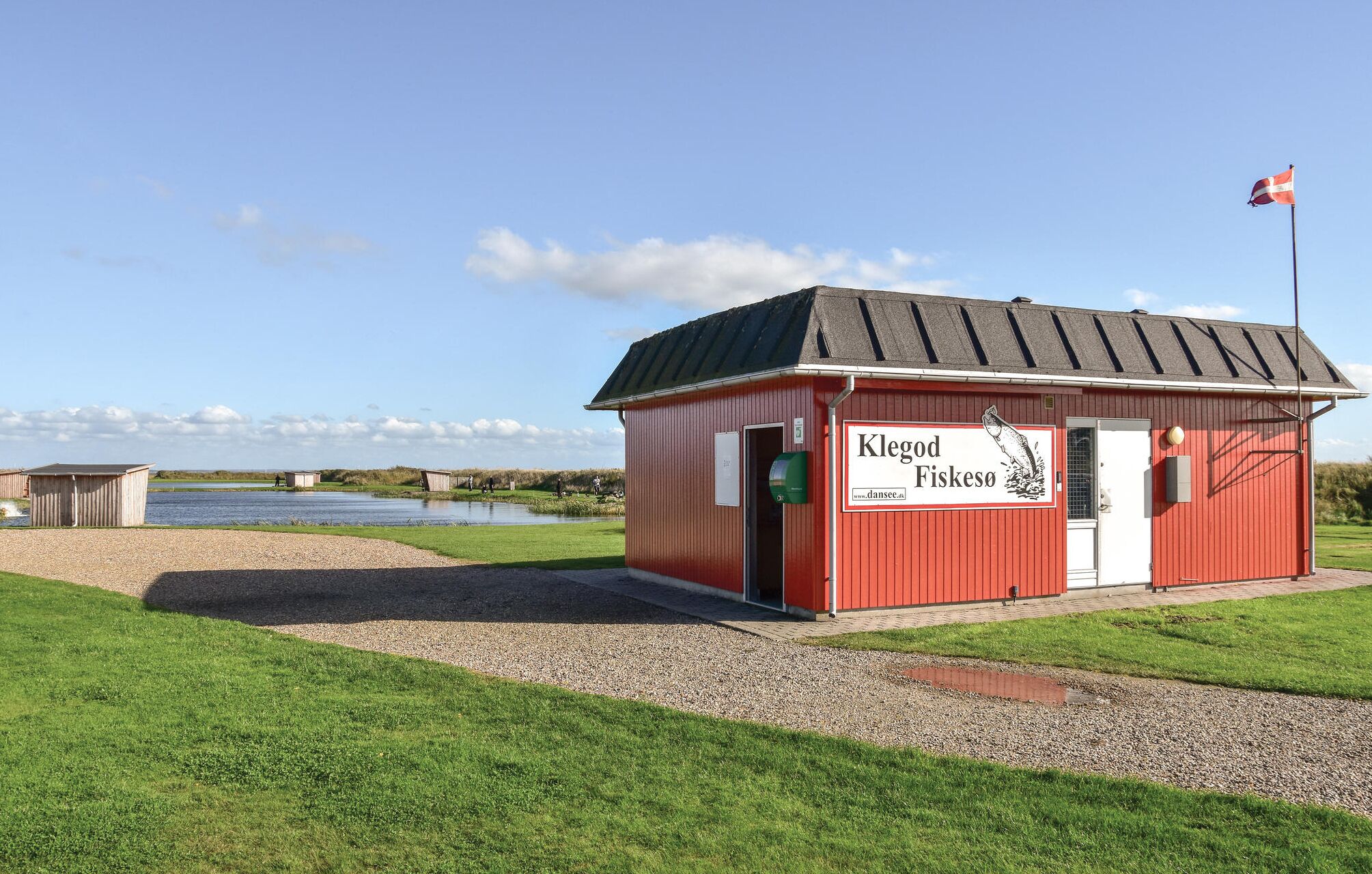 Een rood gebouw met een bord waarop 'Klegod Fiskesø' staat en een vlag erop.