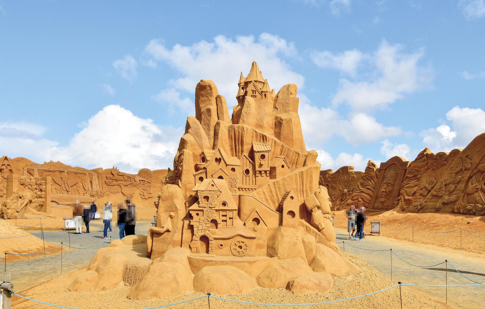 Un castillo de arena grande con múltiples torres y detalles intrincados, rodeado por un paisaje arenoso.