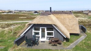 A thatched-roof house with a wooden exterior, a patio with outdoor seating, and a view of the surrounding landscape. - Gorgeous home in Ringkøbing with sauna (Ringkøbing)