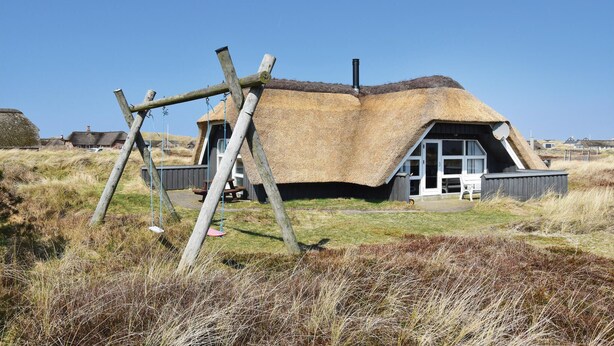 A thatched-roof house with a wooden swing set in front, a chimney, and a clear sky. - Gorgeous home in Ringkøbing with sauna (Ringkøbing)