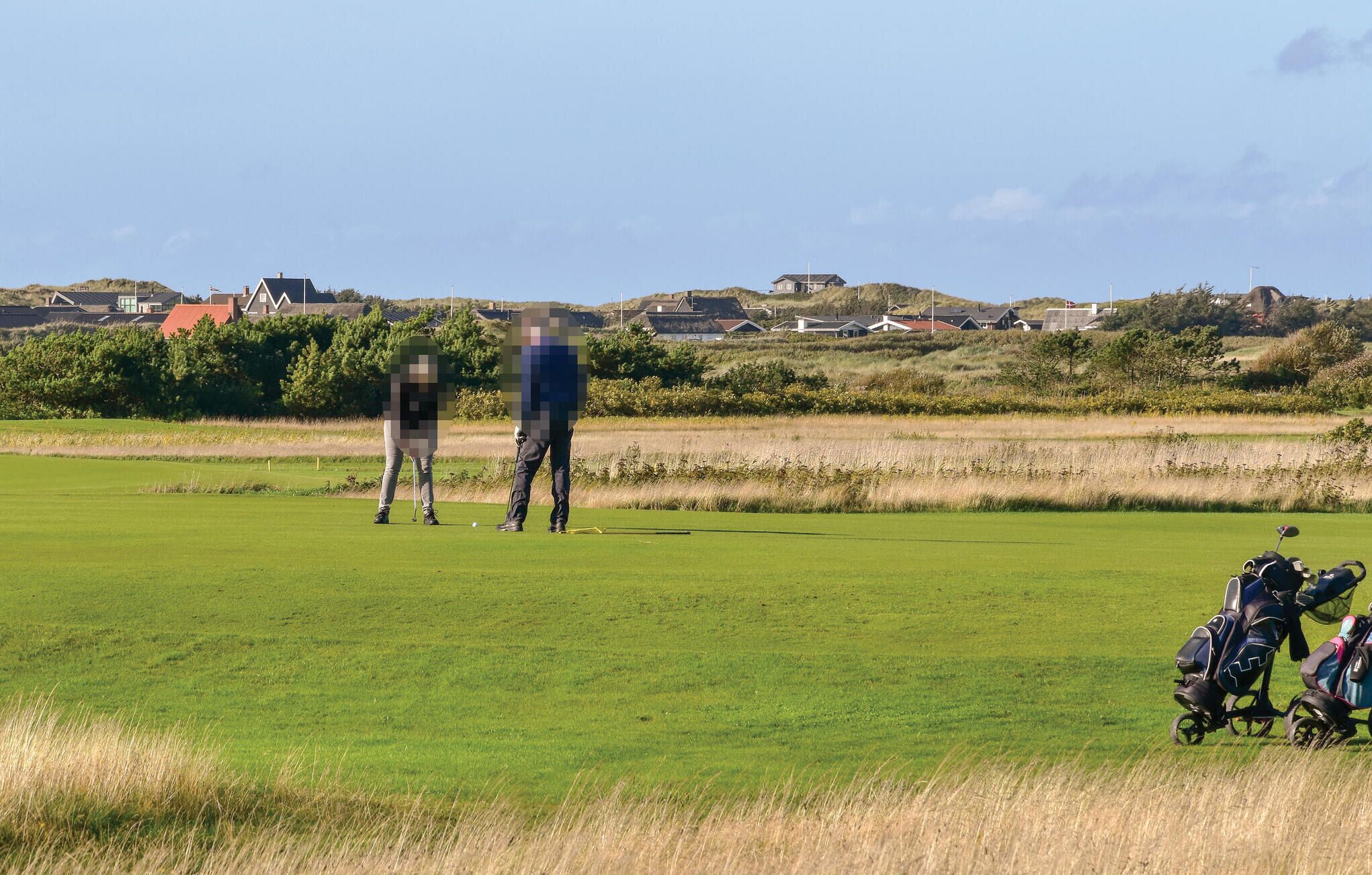 En golfbana med fri sikt över greenen, några golfspelare och en golfbag i förgrunden.