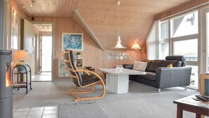 A cozy living room with a wooden ceiling, a black leather sofa, a wooden rocking chair, a white coffee table, and a large window providing natural light. - Gorgeous home in Ringkøbing with sauna (Ringkøbing)