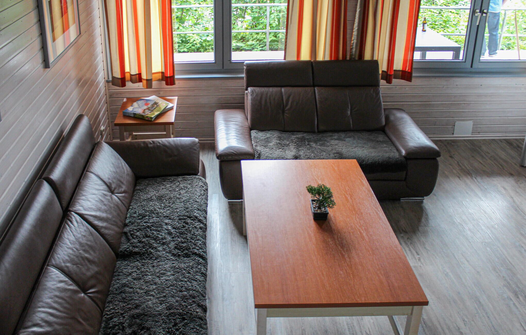 Un salon avec un canapé en cuir marron, un fauteuil en cuir marron et une table basse en bois sur laquelle est posée une petite plante.