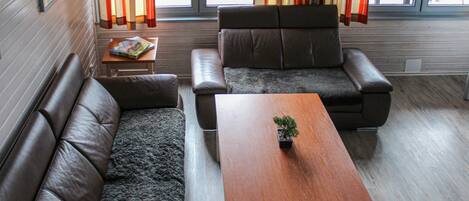 Un salon avec un canapé en cuir marron, un fauteuil en cuir marron et une table basse en bois sur laquelle est posée une petite plante.