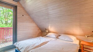 A bedroom with a sloped ceiling, a bed with white linens, a nightstand, and a window with a view of trees.
